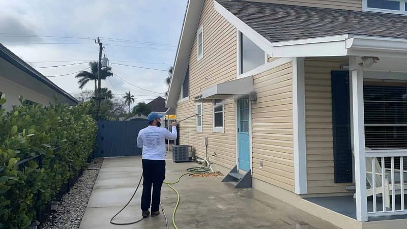 "a man providing house pressure washing via soft washing the vinyl siding of a house in Naples FL"