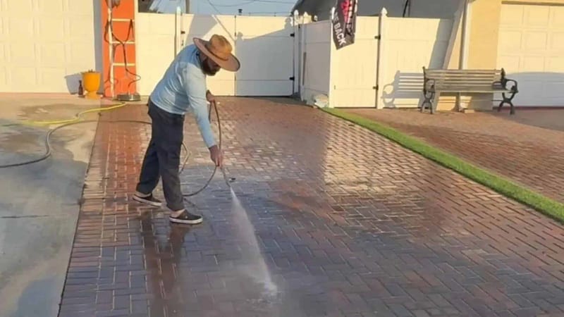 "a man providing paver sealing services using a pressure washer to clean pavers before sealing the surface"